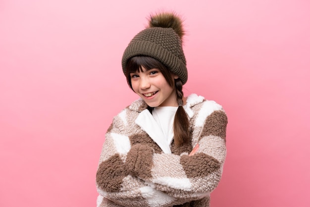 Little caucasian girl with winter jacket isolated on pink background keeping the arms crossed in frontal position