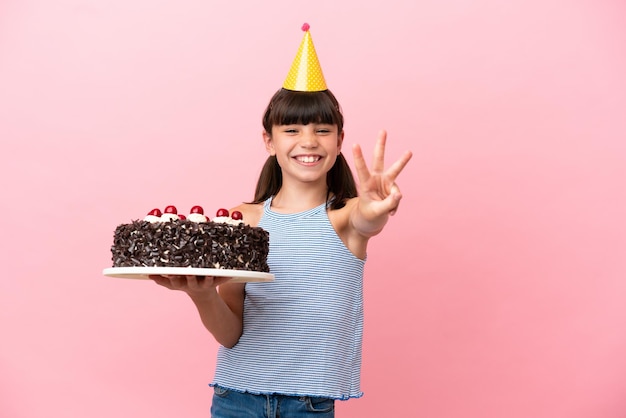 Little caucasian kid holding birthday cake isolated in pink background happy and counting three with fingers