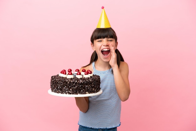 Little caucasian kid holding birthday cake isolated in pink background shouting with mouth wide open