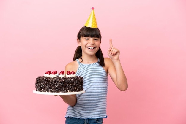 Little caucasian kid holding birthday cake isolated in pink background showing and lifting a finger in sign of the best