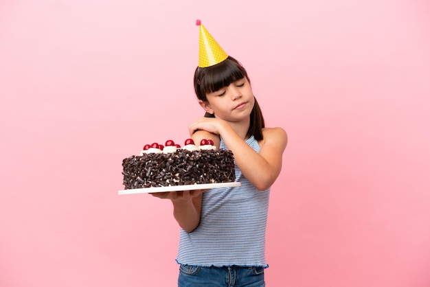 Little caucasian kid holding birthday cake isolated in pink background suffering from pain in shoulder for having made an effort