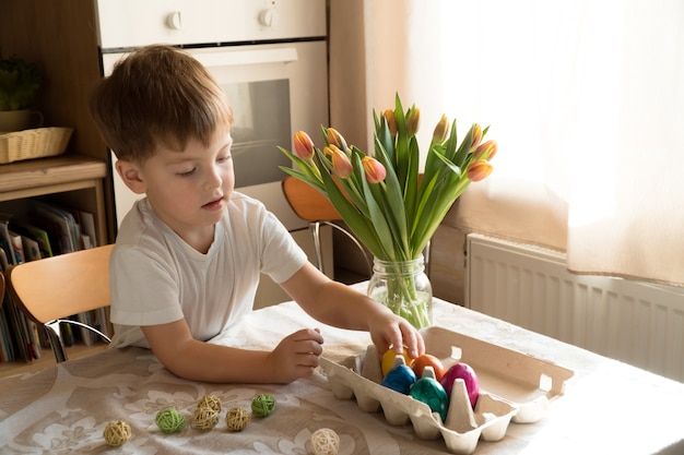 Little caucasian preschool boy playing with colorful easter eggs at home