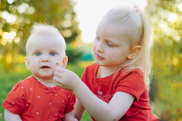 Little caucasian sisters together in park Caucasian blonde girl giving flower to her adorable baby sister