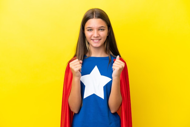 Little caucasian superhero girl isolated on yellow background celebrating a victory in winner position