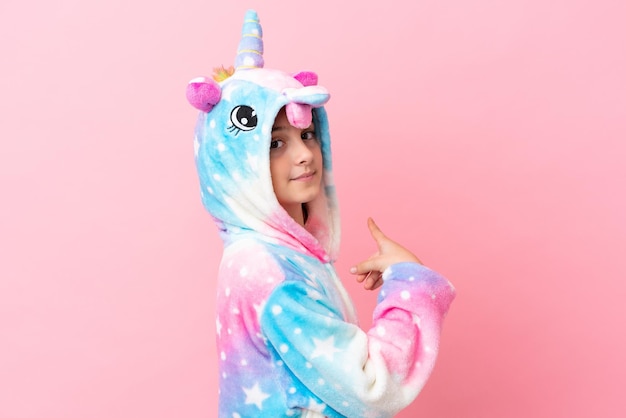 Photo little caucasian woman wearing a unicorn pajama isolated on pink background pointing back