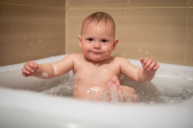 Little charming girl babe plays in the water in a small inflatable baby pool located in the shower stall in the bathroom, baby girl smiling and having fun