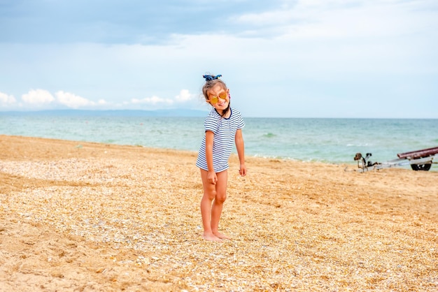 little charming girl in a striped tshirt happily plays on the beach on a sunny day on vacation