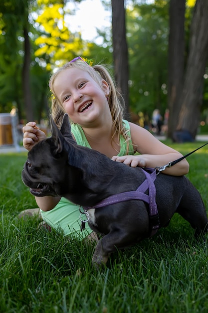 A little cheerful girl hugged a french bulldog dog and laughs merrily