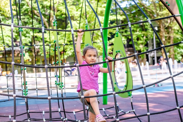 Little cheerful girl plays on vacation in the park at the playground The child is having fun on the street on vacation The child goes in for sports on simulators