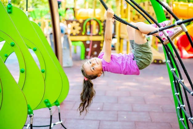 Little cheerful girl plays on vacation in the park at the playground The child is having fun on the street on vacation The child goes in for sports on simulators