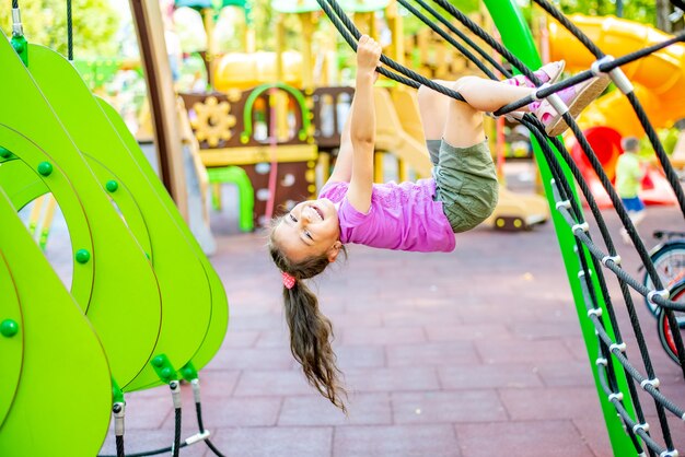 Little cheerful girl plays on vacation in the park at the playground The child is having fun on the street on vacation The child goes in for sports on simulators