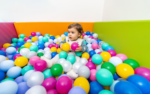 Little cheerful kid lying in playcaenter Child playing in colorful balls