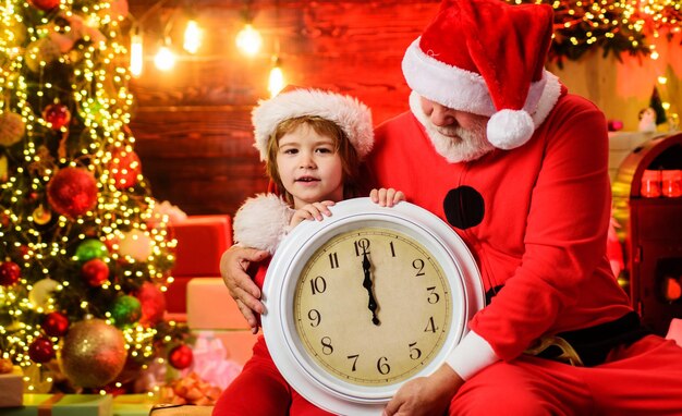 Little child boy and santa claus with old clock waiting for christmas new year midnight