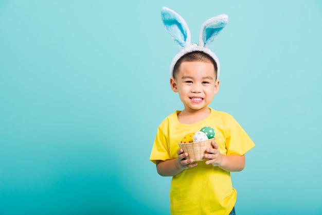 Little child boy wearing bunny ears and yellow T-shirt, hold basket with Easter eggs