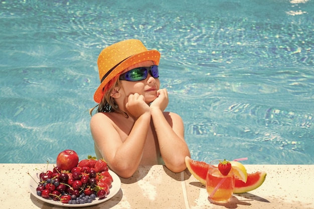 Little child by the pool eating fruit and drinking lemonade cocktail Summer kids vacation concept