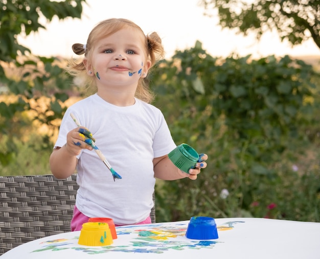 Little child drawing with paint and brush. Cute small girl painting picture in garden, outdoors at home in backyard