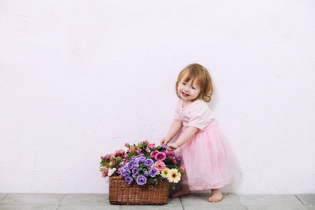 Little child girl beautiful, cute and happy with flowers on white wall background