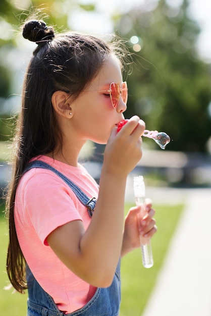 Little child girl blowing soap bubbles in summer park.