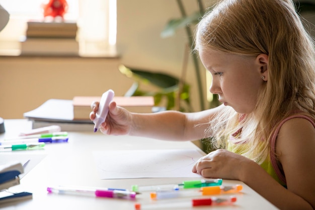 Photo little child girl draws with a marker while sitting at the table