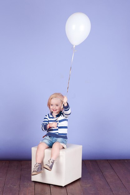 Little child girl holding balloon wear trendy clothes over blue indoor