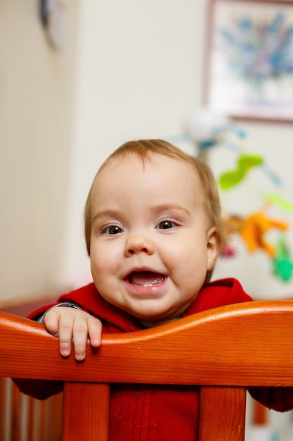 Little child girl in a red sweater, smiles beautifully, in a crib, plays and has fun, emotional photo