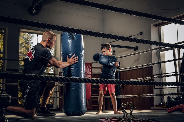 Little child have a serious boxing training with trainer and punching bag.