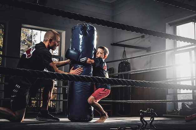 Little child have a serious boxing training with trainer and punching bag.