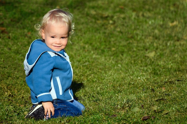 Little child is sitting in the grass and smiling