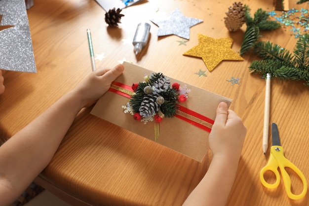 Little child with beautiful Christmas greeting card at wooden table closeup