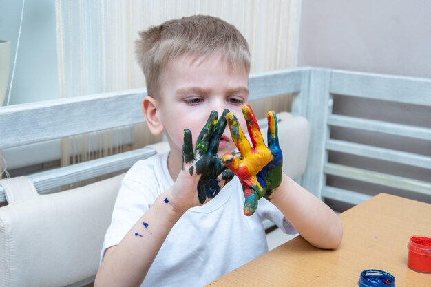 Little child with colorful painted hands. A concentrated boy smears paint on his hands and looks at the result. The child is learning to paint. Learning the basics of color