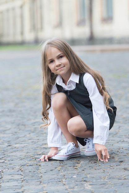 Little child with long hair in school uniform play in schoolyard outdoors, childhood.