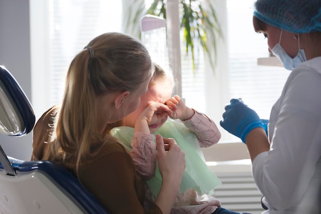 Little child with mommy in stomatology chair - girl is crying, close up