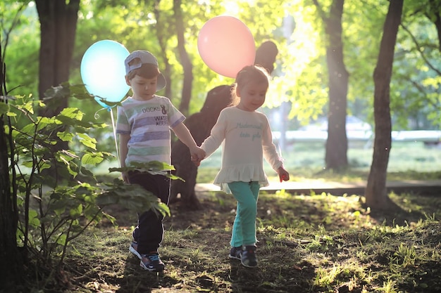 Little children are walking in a park with balloons