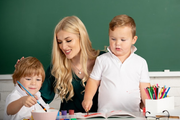 Little children with kindergarten teacher drawing at table indoors learning and playing teacher help