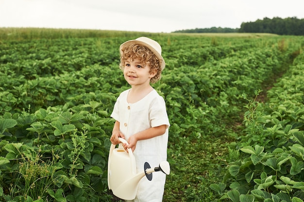 A little curly boy in a white hat and linen clothes in the field