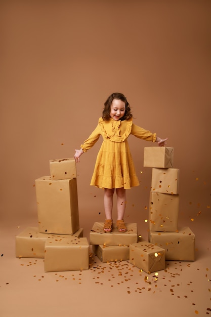 Little curly girl with a stack of gifts for the holiday and gold confetti