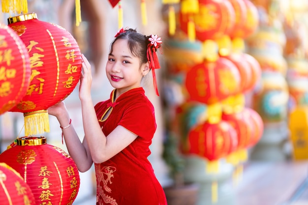 Little Cute Asian girl wearing traditional Chinese cheongsam red with paper lanterns with the Chinese alphabet Blessings written on it Is a Fortune blessing compliment decoration for Chinese New Year