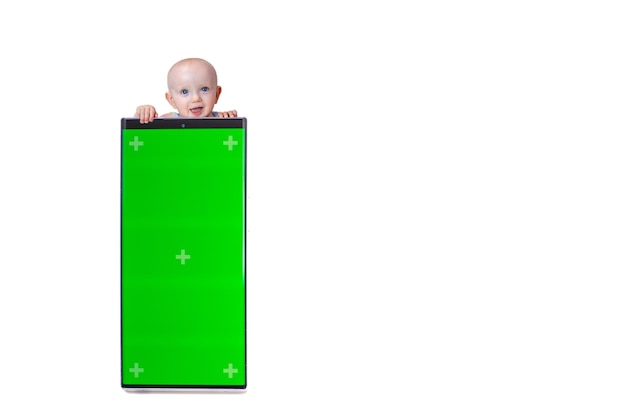 Little cute baby peeking out from behind smartphone with green screen on white background isolate