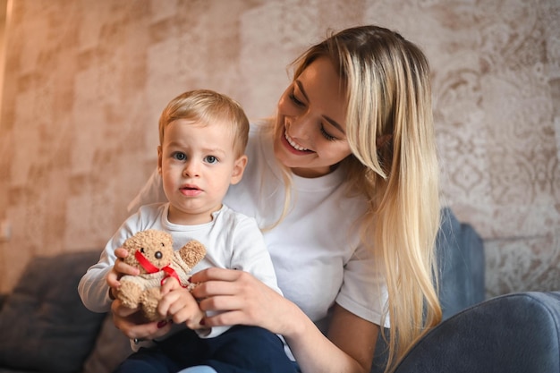 Little cute baby toddler boy blonde sitting on mothers arms beautiful young mom and son playing