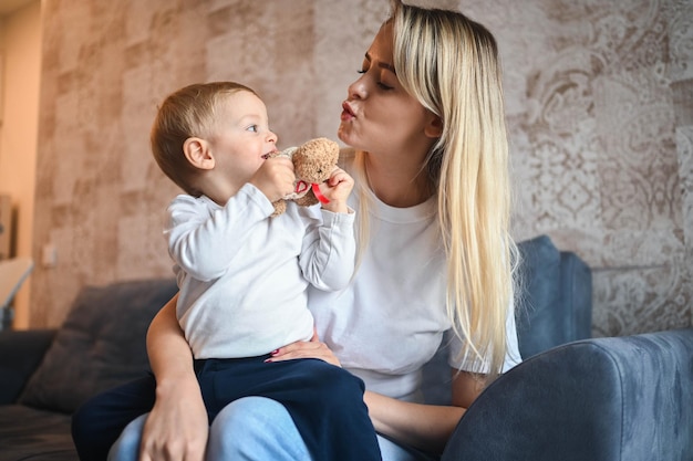 Little cute baby toddler boy blonde sitting on mothers arms beautiful young mom and son playing