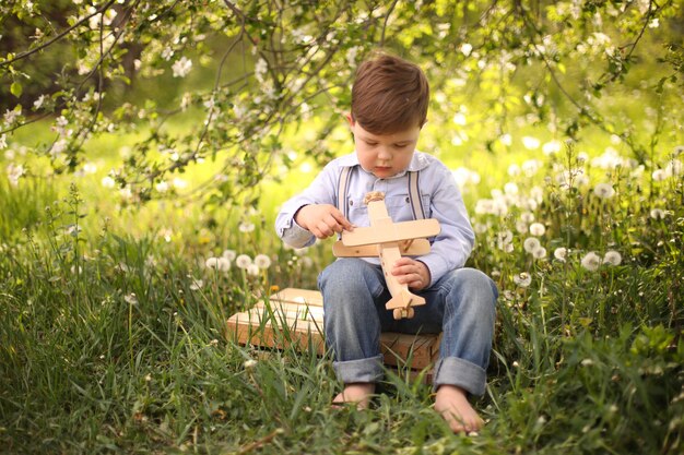 Little cute blond boy playing with a wooden plane in the summer park on the grass on a sunny day