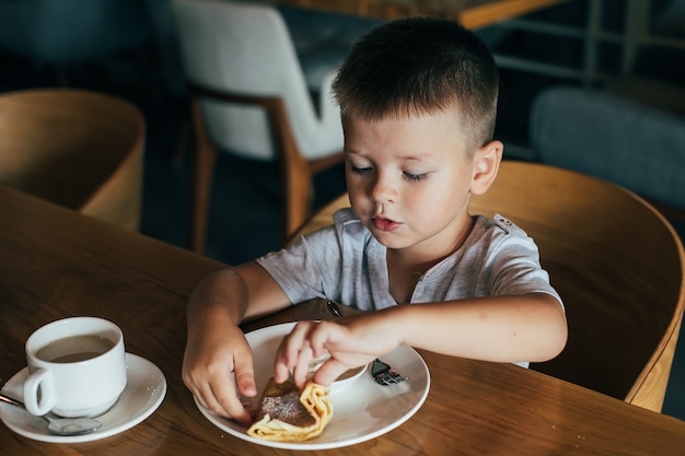 Little and cute boy having breakfast in cafe. 