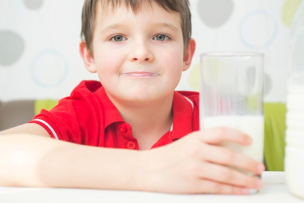 Little cute boy in a red tshirt with a glass of milk in his hand