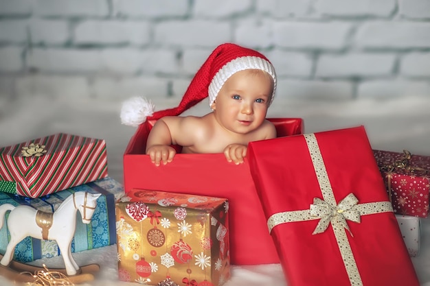 Little cute boy in a Santa hat sits in a gift box Christmas concept