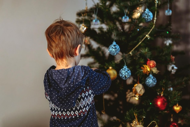 Little cute caucasian boy decorating Christmas tree with twinkling decorations