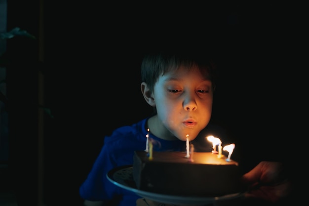 Little cute caucasian boy making a wish puffing out candles on cake on his 9 birthday