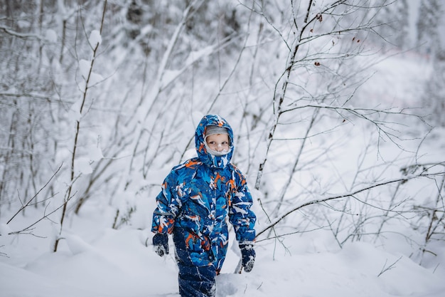 little cute caucasian boy wearing winter overall with hood on and snow on his face in winter forest