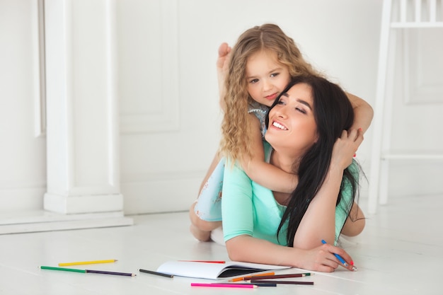 Little cute daughter and her mother drawing with colorful pencils and having fun together. Pretty child and mom playing indoors. Happy family spending time by drawing.