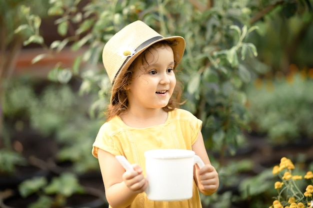 Little cute girl child with water can watering flowers in a garden backyard Kids gardening Outdoors children activity