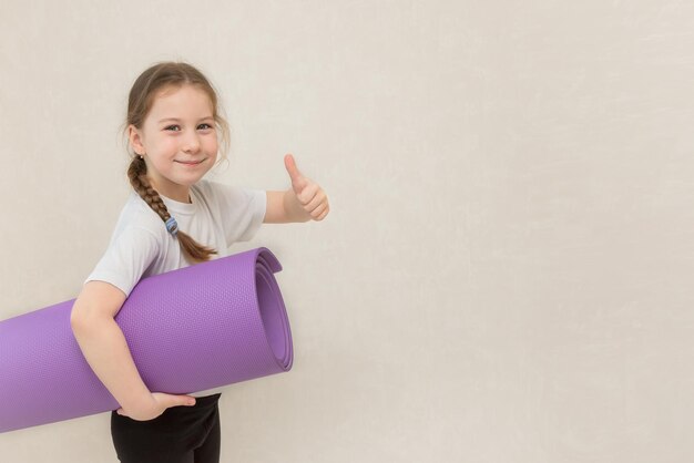 Little cute girl holding a gym mat and showing like copy space sport kids fitness